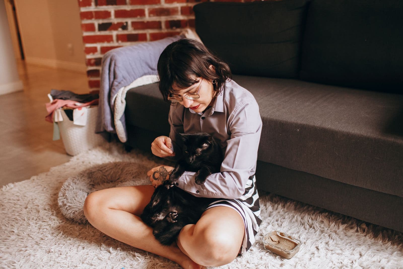 Cuidadora sentada no tapete da sala brincando com um gato preto, em ambiente doméstico
